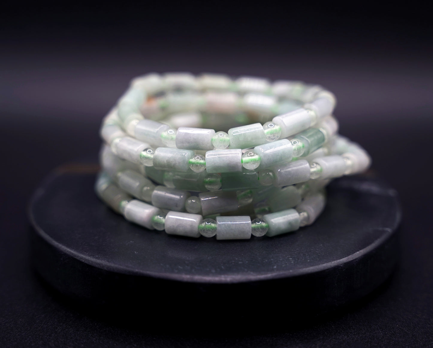 Stack of natural jadeite cylinder bead bracelets in soft green tones, handcrafted healing crystal jewelry on white display