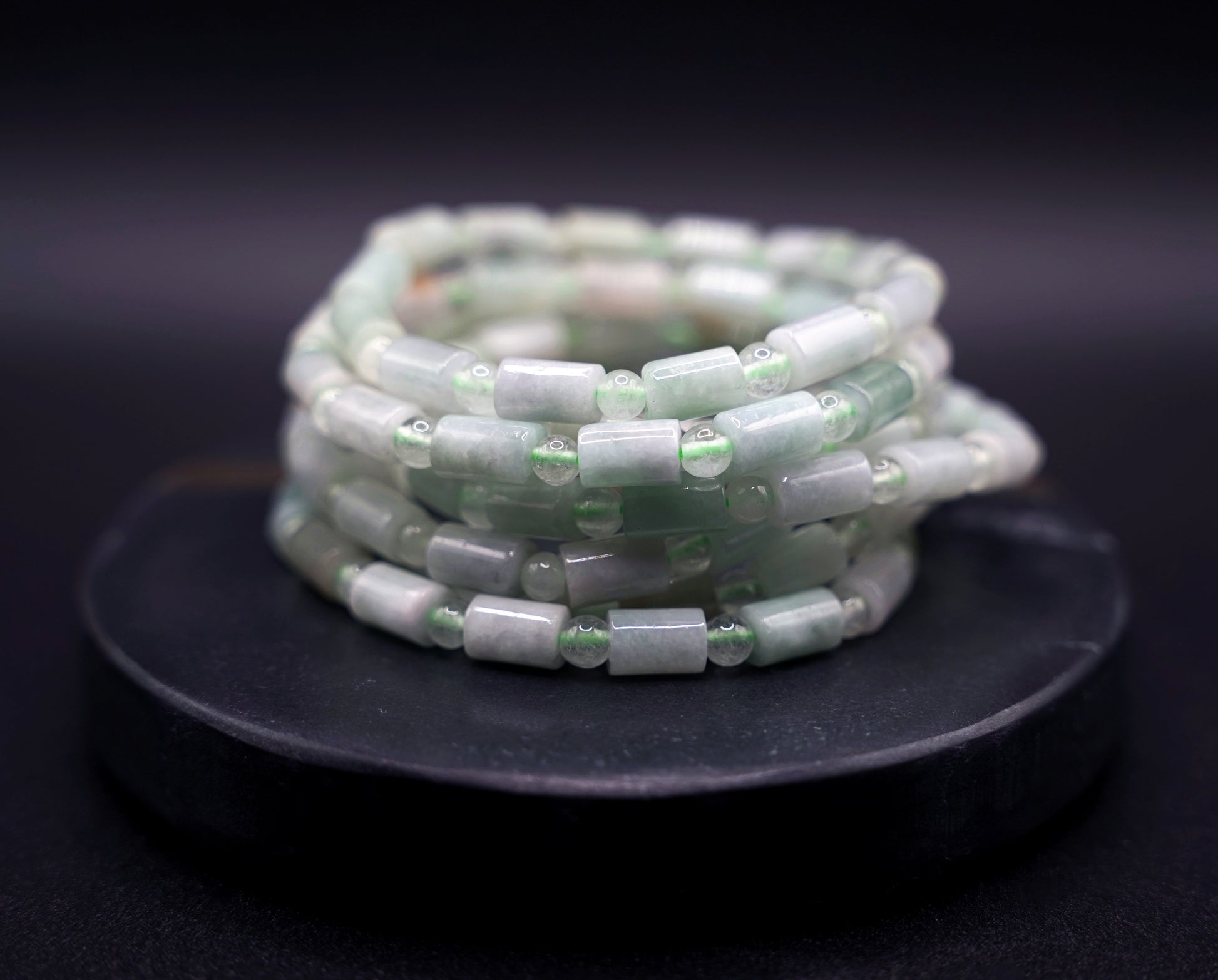 Stack of natural jadeite cylinder bead bracelets in soft green tones, handcrafted healing crystal jewelry on white display