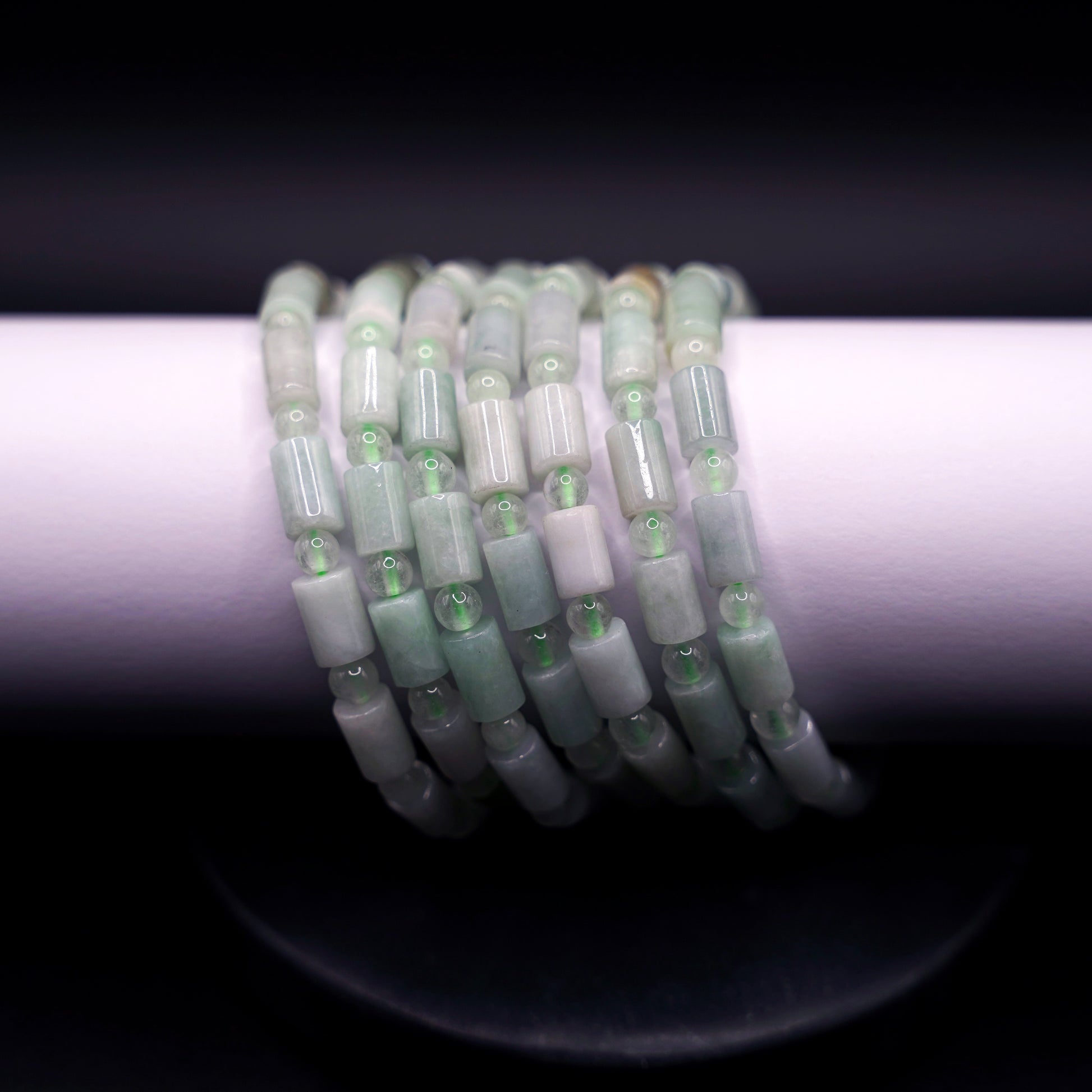 Stack of natural jadeite cylinder bead bracelets in soft green tones, handcrafted healing crystal jewelry on white display