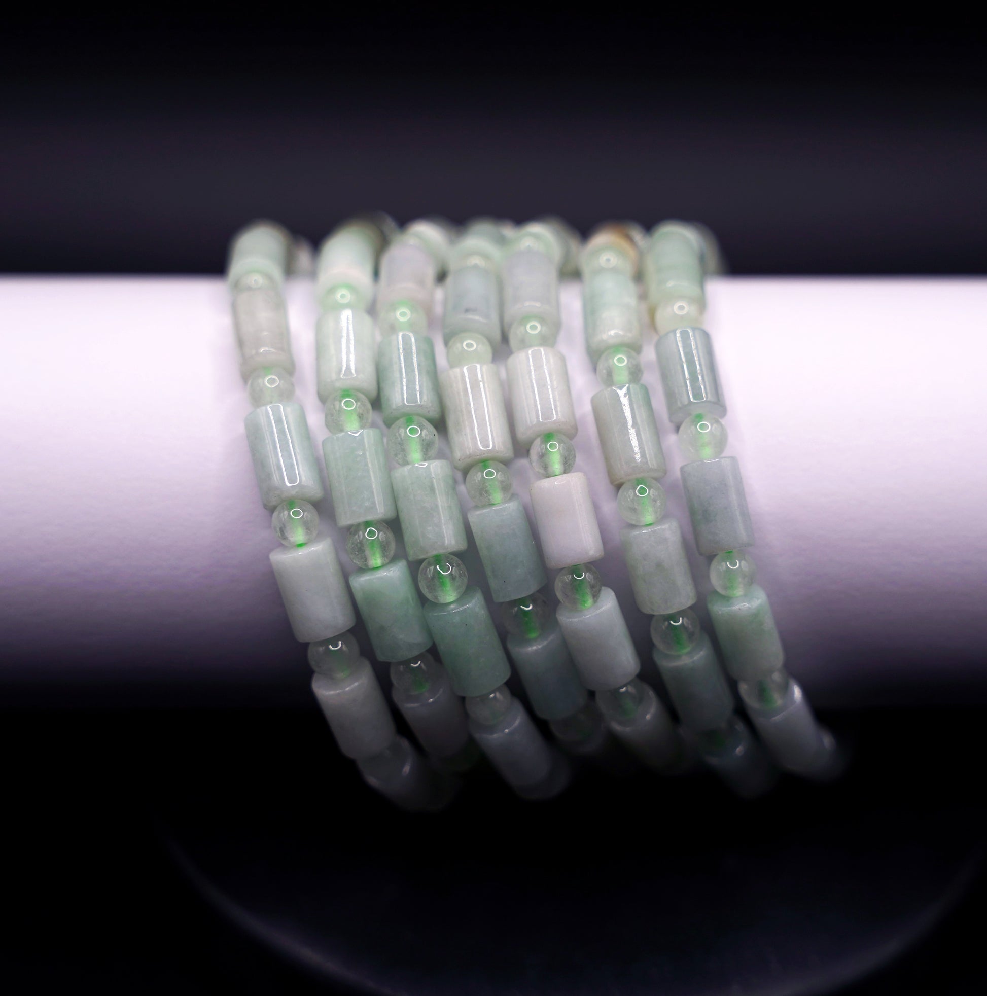 Stack of natural jadeite cylinder bead bracelets in soft green tones, handcrafted healing crystal jewelry on white display