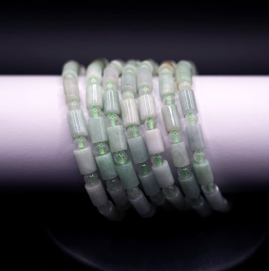 Stack of natural jadeite cylinder bead bracelets in soft green tones, handcrafted healing crystal jewelry on white display
