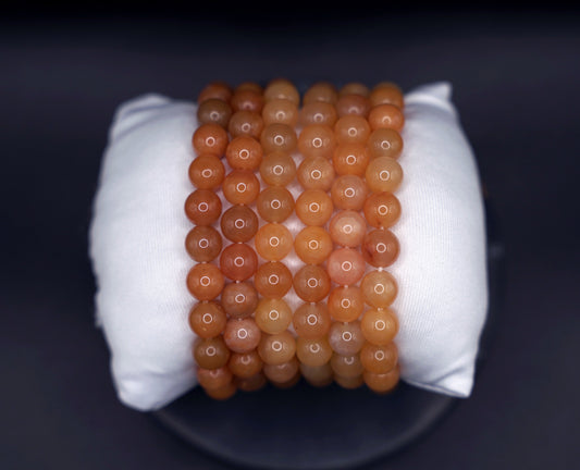 Stack of natural yellow jade round bead bracelets displayed on a white cushion, polished gemstone crystal jewelry
